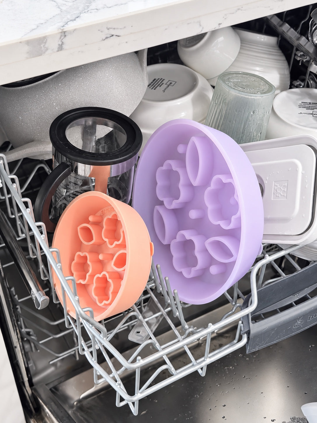 Purple and peach Flower and Leaf slow feeder bowls arranged in a dishwasher rack.