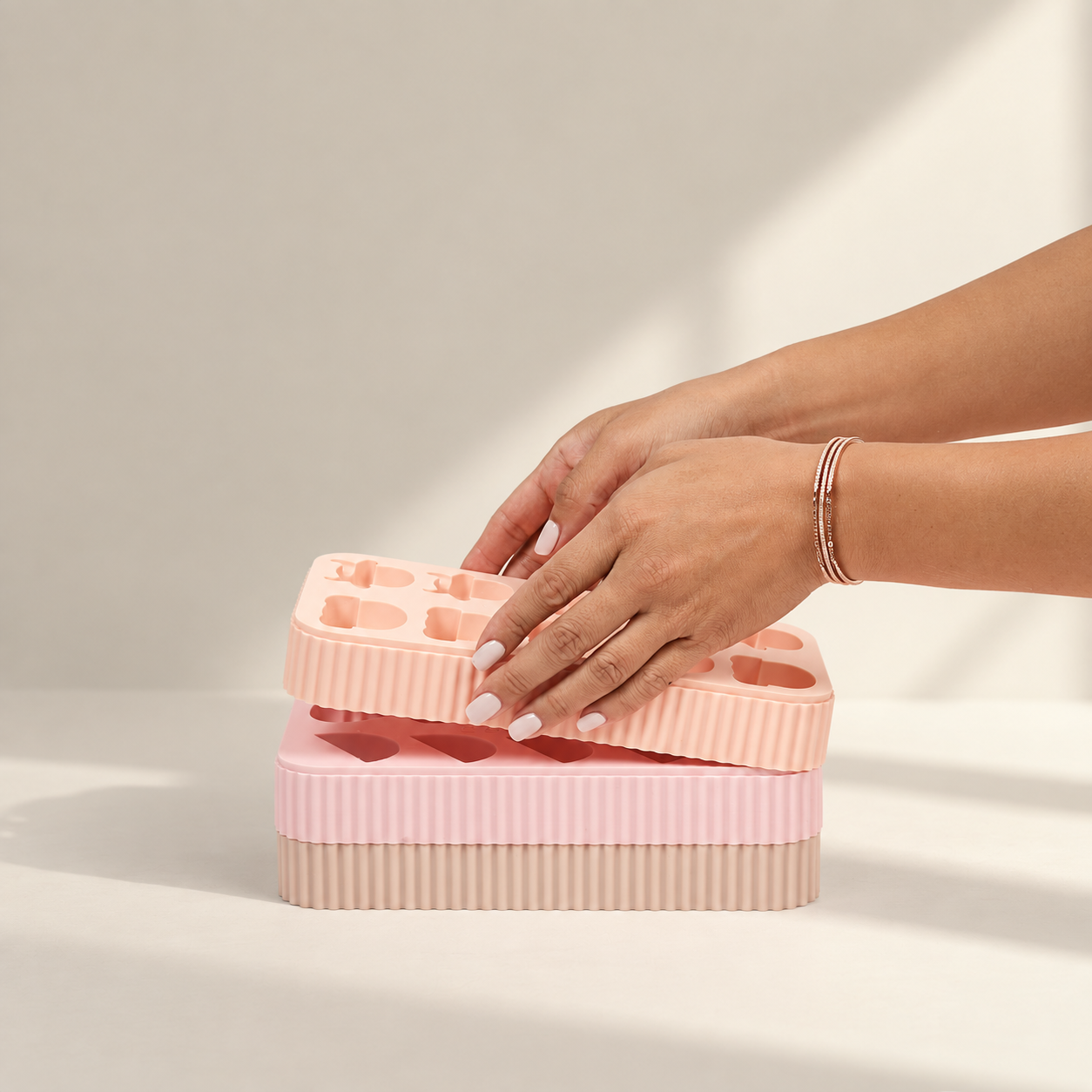 Hands stacking silicone treat molds to demonstrate space-saving storage.